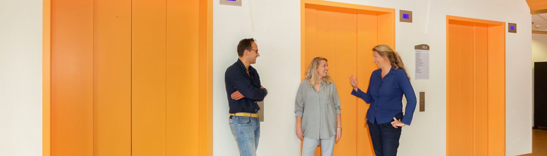Drie personen staan bij de liften te praten met elkaar Drie personen staan bij de liften te praten met elkaar